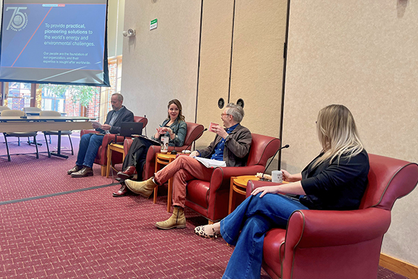Four EERC employees sit in red leather chairs and appear to be mid-discussion. The EERC's mission statement is projected in the background.