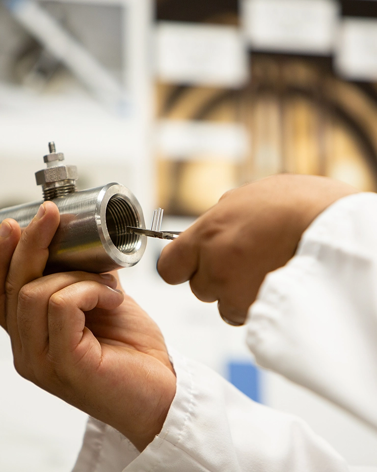 A person in a lab coat, holding a metal pipe and three small tubes