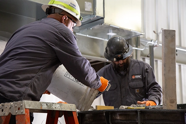 two men in hard hats pouring from a bucket