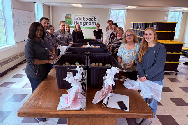 13 people standing around a table topped with bins of food.