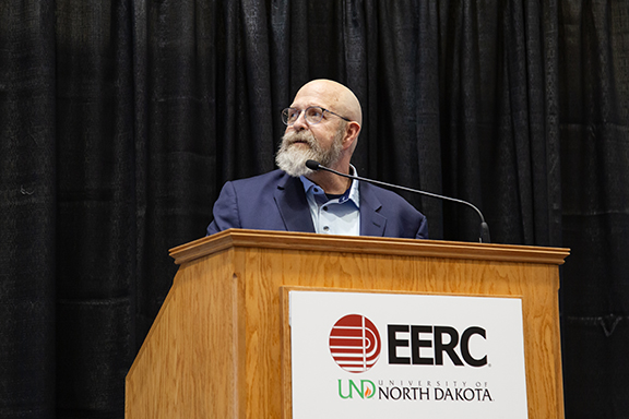Man in a blue sport coat and glasses stands at a podium and looks off into the distance.